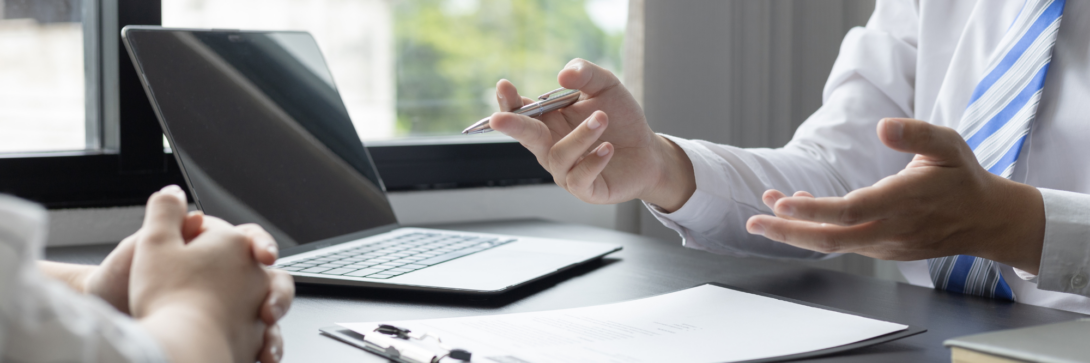 Zwei Personen im Gespräch am Schreibtisch mit Laptop und Unterlagen – symbolisch für digitale Personalverwaltung und moderne HR-Prozesse.