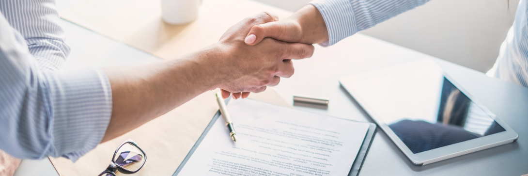 Zwei Personen reichen sich beim Vertragsabschluss die Hand, daneben liegen Vertrag, Stift und Tablet – Symbolbild für einen zuverlässigen Vertragsmanagement Anbieter.