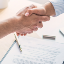 Zwei Personen reichen sich beim Vertragsabschluss die Hand, daneben liegen Vertrag, Stift und Tablet – Symbolbild für einen zuverlässigen Vertragsmanagement Anbieter.
