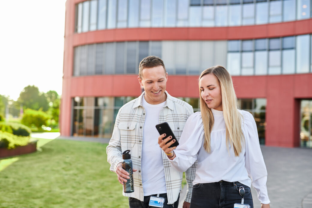 Zwei Mitarbeiter schauen auf ein Handy an ihrem Modern Workplace bei d.velop