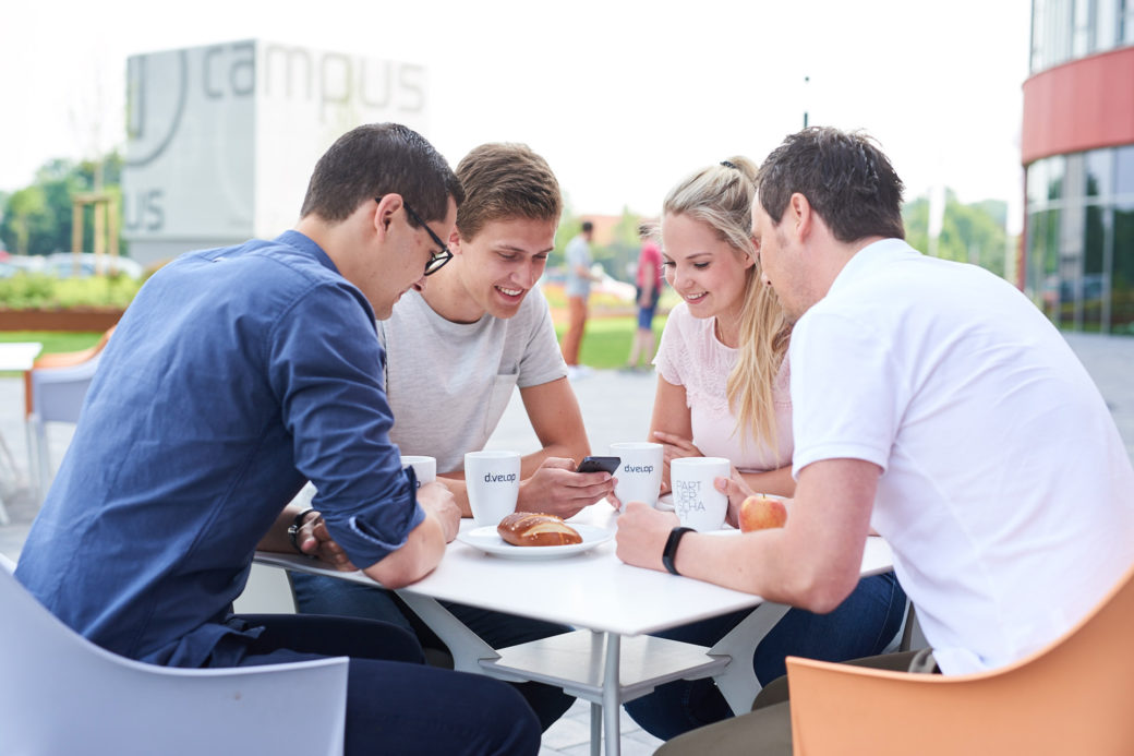 d-velop Mitarbeiter draußen Sitzgruppe mit Smartphone und Kaffee