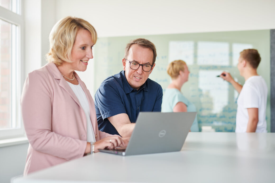 Frau und Mann, die vor einem Laptop stehen schauen ein Webinar zum Thema Dokumente digitalisieren 