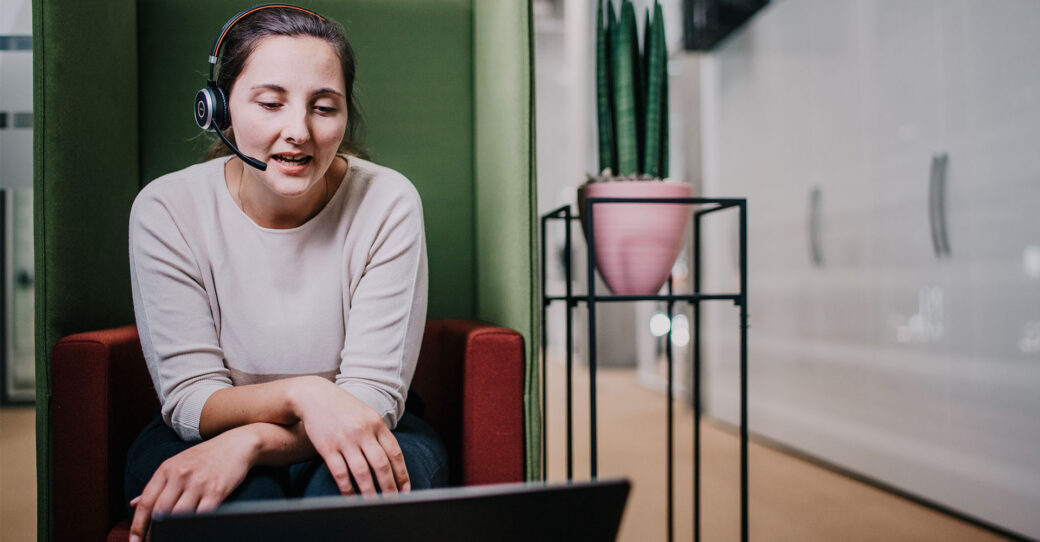 Mitarbeiterin mit Headset am Arbeiten vor dem Laptop