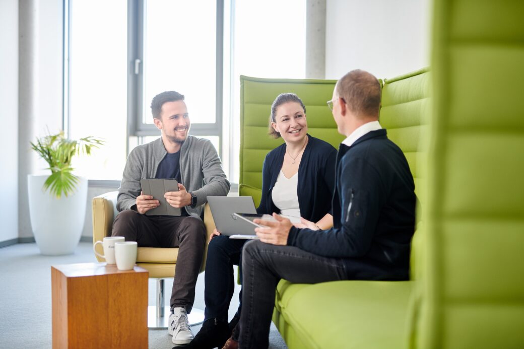 Drei Personen schauen sich ein Whitepaper auf einem Laptop an