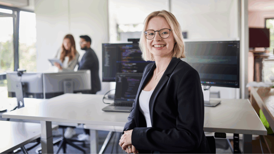 Lächelnde Person vor einem Rechner-Arbeitsplatz