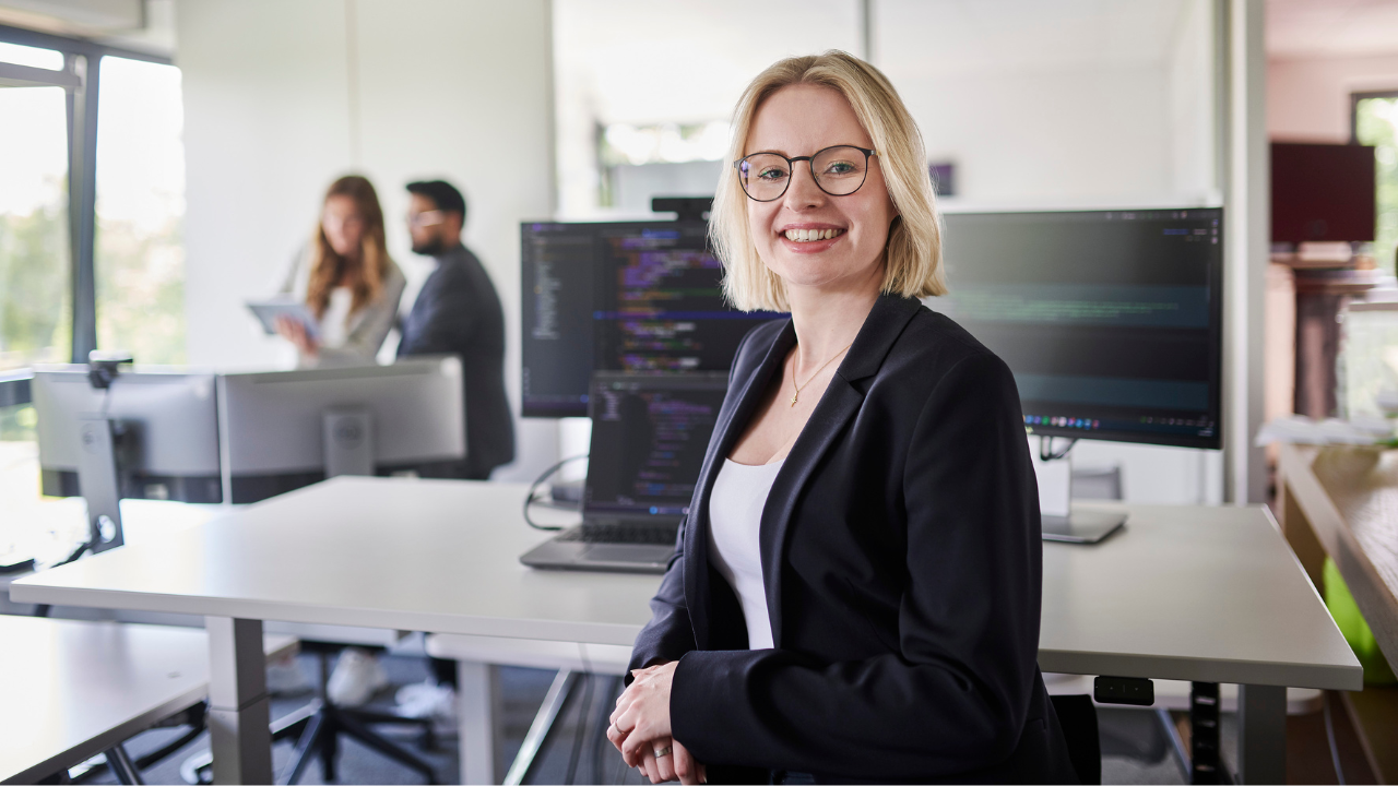 Lächelnde Person vor einem Rechner-Arbeitsplatz